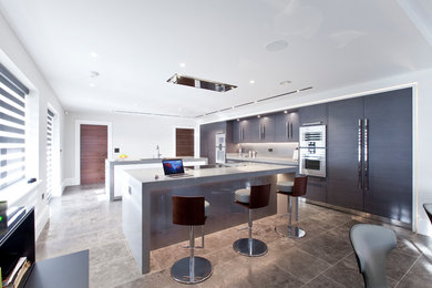 Large contemporary open plan kitchen in Cheshire with a submerged sink, flat-panel cabinets, grey cabinets, quartz worktops, metallic splashback, glass sheet splashback, stainless steel appliances, limestone flooring and multiple islands.