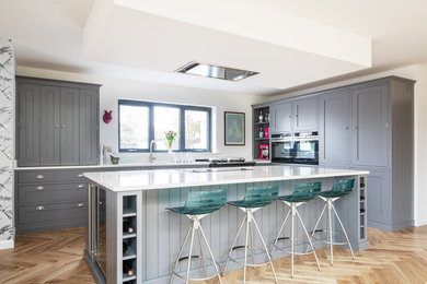 Large traditional l-shaped open plan kitchen in Devon with a submerged sink, shaker cabinets, grey cabinets, composite countertops, light hardwood flooring, an island, brown floors and white worktops.