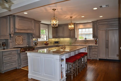 Example of a mid-sized transitional l-shaped medium tone wood floor eat-in kitchen design in Houston with a double-bowl sink, raised-panel cabinets, gray cabinets, granite countertops, white backsplash, stone slab backsplash, paneled appliances and an island