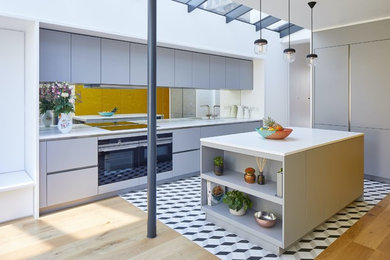 Moderne Küche mit Waschbecken, flächenbündigen Schrankfronten, grauen Schränken, Rückwand aus Spiegelfliesen, Kücheninsel, buntem Boden und weißer Arbeitsplatte in London