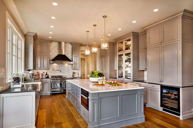 Inspiration for a mid-sized timeless u-shaped light wood floor enclosed kitchen remodel in Portland with a farmhouse sink, recessed-panel cabinets, gray cabinets, quartz countertops, white backsplash, stone tile backsplash, black appliances and an island