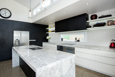 Example of a mid-sized trendy l-shaped concrete floor eat-in kitchen design in Auckland with an undermount sink, flat-panel cabinets, white cabinets, granite countertops, white backsplash, ceramic backsplash, stainless steel appliances and an island