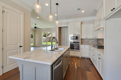 Inredning av ett kök, med vita skåp, granitbänkskiva, rostfria vitvaror, mellanmörkt trägolv och en köksö