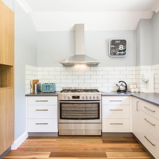 Inspiration for a mid-sized transitional u-shaped eat-in kitchen in Canberra - Queanbeyan with a drop-in sink, flat-panel cabinets, white cabinets, laminate benchtops, white splashback, porcelain splashback, stainless steel appliances, medium hardwood floors, beige floor and no island.