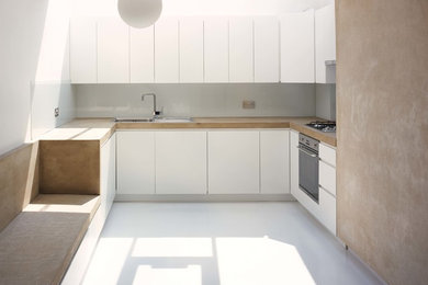 Foto på ett mellanstort funkis kök, med en nedsänkt diskho, släta luckor, vita skåp, bänkskiva i betong, vitt stänkskydd, glaspanel som stänkskydd, rostfria vitvaror och linoleumgolv