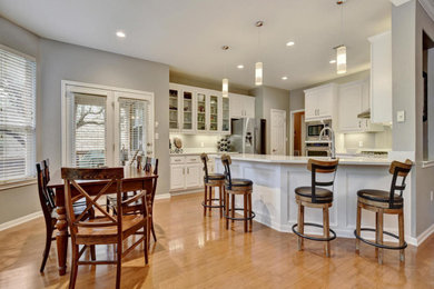 Mid-sized arts and crafts l-shaped light wood floor and beige floor eat-in kitchen photo in Austin with an undermount sink, raised-panel cabinets, white cabinets, quartz countertops, white backsplash, stainless steel appliances and white countertops
