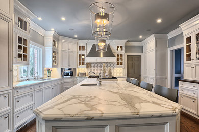 Example of a large classic u-shaped medium tone wood floor open concept kitchen design in Other with an undermount sink, shaker cabinets, white cabinets, marble countertops, white backsplash, stone tile backsplash, stainless steel appliances and an island
