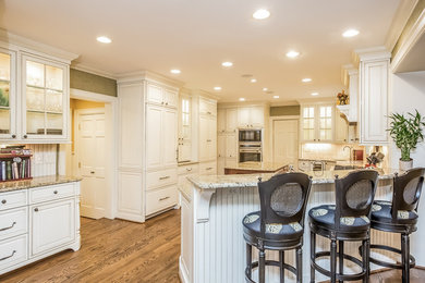 Example of a large classic medium tone wood floor eat-in kitchen design in Detroit with an undermount sink, raised-panel cabinets, white cabinets, granite countertops, white backsplash, stainless steel appliances and an island