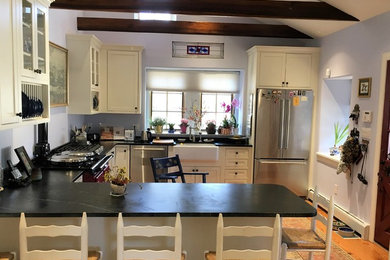 Example of a mid-sized cottage u-shaped light wood floor and brown floor kitchen pantry design in Philadelphia with a farmhouse sink, shaker cabinets, white cabinets, soapstone countertops, stainless steel appliances and an island