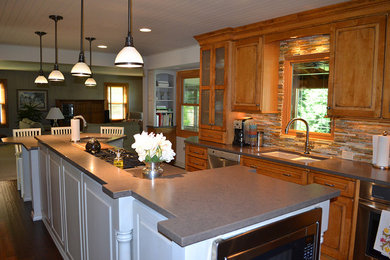Example of a large classic l-shaped medium tone wood floor eat-in kitchen design in Columbus with an undermount sink, raised-panel cabinets, medium tone wood cabinets, solid surface countertops, multicolored backsplash, stone tile backsplash, stainless steel appliances and an island