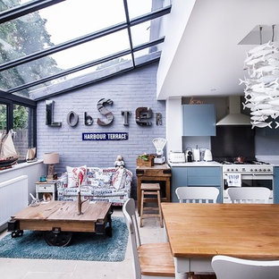 Inspiration for a medium sized nautical l-shaped open plan kitchen in London with an integrated sink, flat-panel cabinets, blue cabinets, composite countertops, grey splashback, glass sheet splashback, white appliances, travertine flooring, beige floors, white worktops and no island.