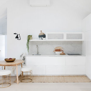 Design ideas for a beach style l-shaped open plan kitchen in Sydney with a single-bowl sink, shaker cabinets, white cabinets, white appliances, no island, grey splashback, light hardwood floors, beige floor and grey benchtop.