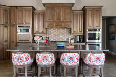 French country medium tone wood floor and brown floor kitchen photo in Dallas with an undermount sink, raised-panel cabinets, medium tone wood cabinets, granite countertops, multicolored backsplash, ceramic backsplash, stainless steel appliances, an island and multicolored countertops