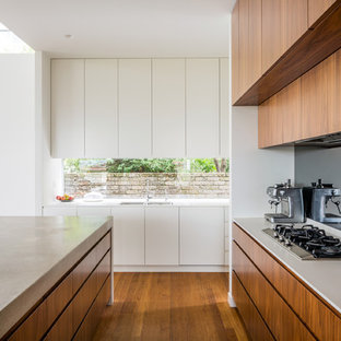 This is an example of a contemporary l-shaped kitchen in Sydney with medium wood cabinets, medium hardwood floors, with island, a double-bowl sink, flat-panel cabinets, window splashback, stainless steel appliances, brown floor and white benchtop.
