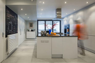 Design ideas for a large contemporary galley open plan kitchen in London with a submerged sink, flat-panel cabinets, white cabinets, granite worktops, stainless steel appliances, ceramic flooring and an island.