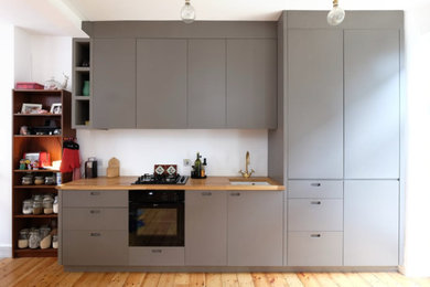 Scandinavian galley kitchen/diner in London with a built-in sink, flat-panel cabinets, grey cabinets, wood worktops, white splashback, black appliances, light hardwood flooring and no island.