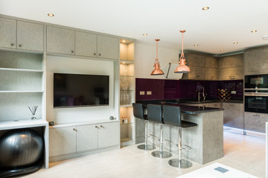 Contemporary u-shaped open plan kitchen in London with a built-in sink, flat-panel cabinets, grey cabinets, composite countertops, stainless steel appliances, ceramic flooring, a breakfast bar, white floors and black worktops.