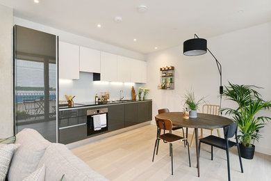 This is an example of a small contemporary single-wall kitchen in London with a submerged sink, flat-panel cabinets, grey cabinets, stainless steel appliances, light hardwood flooring and white floors.