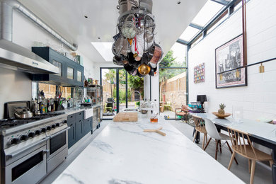 Eclectic galley kitchen/diner in London with a belfast sink, shaker cabinets, black cabinets, stainless steel appliances, concrete flooring, an island, grey floors and grey worktops.