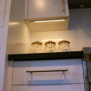This is an example of a small modern galley eat-in kitchen in New York with an undermount sink, flat-panel cabinets, white cabinets, solid surface benchtops, subway tile splashback, stainless steel appliances, ceramic floors and with island.
