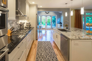Eat-in kitchen - mid-sized transitional galley light wood floor eat-in kitchen idea in Orange County with an undermount sink, shaker cabinets, white cabinets, granite countertops, gray backsplash, stone tile backsplash, stainless steel appliances and an island