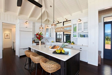 Large island style l-shaped dark wood floor and black floor open concept kitchen photo in Hawaii with a farmhouse sink, shaker cabinets, white cabinets, white backsplash, paneled appliances, an island, marble countertops and mosaic tile backsplash