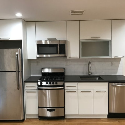 Example of a small trendy single-wall medium tone wood floor and brown floor eat-in kitchen design in New York with an undermount sink, flat-panel cabinets, white cabinets, quartz countertops, white backsplash, ceramic backsplash, stainless steel appliances and no island