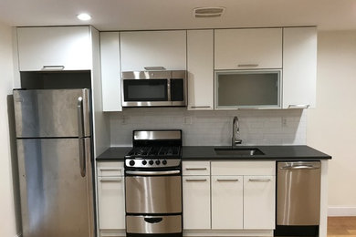 Example of a small trendy single-wall medium tone wood floor and brown floor eat-in kitchen design in New York with an undermount sink, flat-panel cabinets, white cabinets, quartz countertops, white backsplash, ceramic backsplash, stainless steel appliances and no island