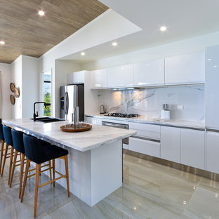 Inspiration for a contemporary galley eat-in kitchen in Brisbane with a double-bowl sink, flat-panel cabinets, white cabinets, white splashback, stainless steel appliances, with island, beige floor and white benchtop.