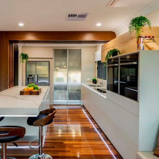Design ideas for a large contemporary l-shaped eat-in kitchen in Brisbane with flat-panel cabinets, beige cabinets, quartz benchtops, black appliances, medium hardwood floors, with island, brown floor and white benchtop.