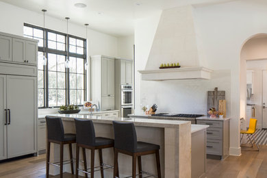 Inspiration for a mid-sized mediterranean l-shaped light wood floor kitchen remodel in Austin with shaker cabinets, gray cabinets, white backsplash, paneled appliances, an island, granite countertops and glass tile backsplash