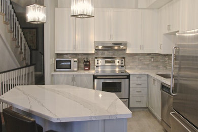Inspiration for a transitional l-shaped ceramic tile open concept kitchen remodel in Toronto with a double-bowl sink, shaker cabinets, white cabinets, quartz countertops, gray backsplash, mosaic tile backsplash, stainless steel appliances and an island