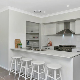 Design ideas for a mid-sized contemporary kitchen in Central Coast with a drop-in sink, flat-panel cabinets, white cabinets, white splashback, stainless steel appliances, a peninsula, grey floor and white benchtop.