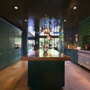 Design ideas for a large classic galley kitchen/diner in London with a submerged sink, shaker cabinets, blue cabinets, granite worktops, green splashback, metro tiled splashback, stainless steel appliances, medium hardwood flooring, an island, brown floors and black worktops.