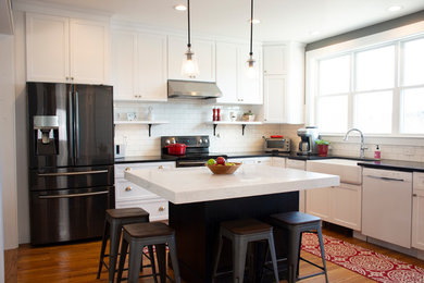 Example of a mid-sized classic l-shaped medium tone wood floor and brown floor kitchen design in Boston with a farmhouse sink, shaker cabinets, white cabinets, granite countertops, white backsplash, ceramic backsplash, an island and black countertops