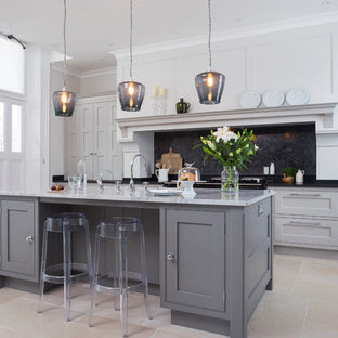 Large transitional open plan kitchen in Hampshire with grey cabinets, black splashback, with island, a double-bowl sink, beaded inset cabinets, granite benchtops and limestone floors.