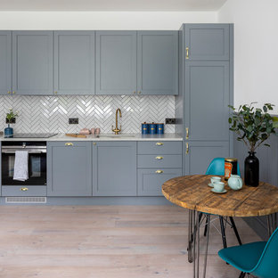Inspiration for a small contemporary single-wall kitchen/diner in Hertfordshire with a submerged sink, shaker cabinets, grey cabinets, quartz worktops, white splashback, black appliances, no island, white worktops, medium hardwood flooring and beige floors.