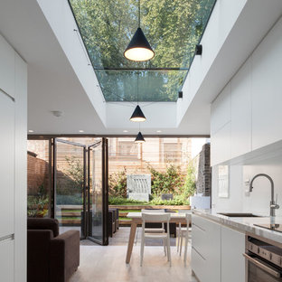 This is an example of a contemporary galley kitchen in London with a submerged sink, flat-panel cabinets, white cabinets, stainless steel appliances, no island, marble worktops, white splashback and ceramic flooring.