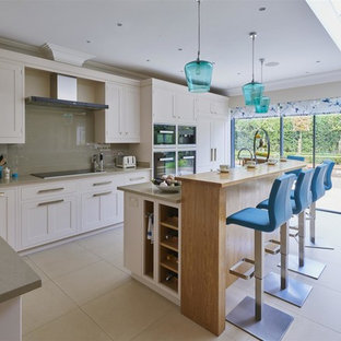This is an example of a mid-sized transitional l-shaped kitchen in Surrey with shaker cabinets, quartzite benchtops, with island, beige cabinets, grey splashback, glass sheet splashback, black appliances, beige floor and grey benchtop.
