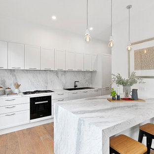 Inspiration for a mid-sized transitional single-wall open plan kitchen in Melbourne with a drop-in sink, white cabinets, marble benchtops, grey splashback, marble splashback, with island, grey benchtop, black appliances, medium hardwood floors and brown floor.