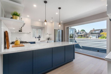 Enclosed kitchen - mid-sized coastal u-shaped light wood floor and beige floor enclosed kitchen idea in Vancouver with a farmhouse sink, shaker cabinets, blue cabinets, quartz countertops, white backsplash, ceramic backsplash, stainless steel appliances, a peninsula and white countertops