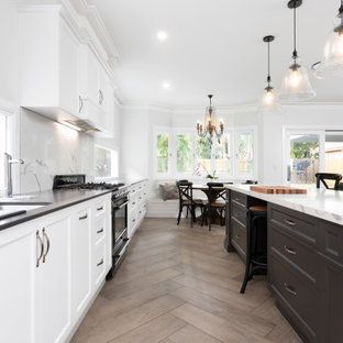 Inspiration for a large beach style open plan kitchen in Brisbane with an undermount sink, shaker cabinets, white cabinets, granite benchtops, stone slab splashback, black appliances, ceramic floors, with island, brown floor and black benchtop.