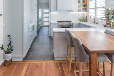 Inspiration för mellanstora moderna vitt kök, med en undermonterad diskho, luckor med infälld panel, grå skåp, bänkskiva i kvarts, vitt stänkskydd, stänkskydd i tunnelbanekakel, rostfria vitvaror, klinkergolv i porslin, en halv köksö och grått golv