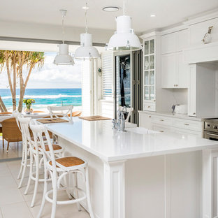 Large beach style galley eat-in kitchen in Gold Coast - Tweed with a farmhouse sink, white cabinets, marble benchtops, white splashback, marble splashback, stainless steel appliances, ceramic floors, with island, beige floor, white benchtop and recessed-panel cabinets.