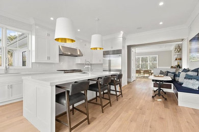 Open concept kitchen - large transitional l-shaped light wood floor and brown floor open concept kitchen idea in New York with an undermount sink, shaker cabinets, white cabinets, quartz countertops, white backsplash, matchstick tile backsplash, stainless steel appliances and an island