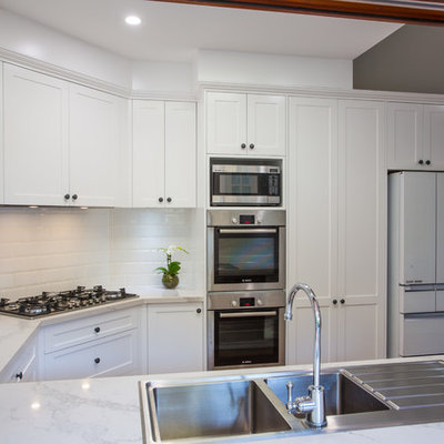Example of a large classic u-shaped medium tone wood floor and brown floor open concept kitchen design in Brisbane with a double-bowl sink, shaker cabinets, white cabinets, quartz countertops, white backsplash, subway tile backsplash, stainless steel appliances and an island