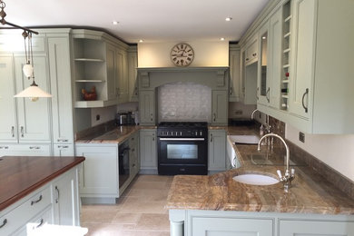 Inspiration for a large traditional l-shaped enclosed kitchen in Hampshire with a belfast sink, beaded cabinets, green cabinets, granite worktops, beige splashback, black appliances, limestone flooring, an island, stone slab splashback, beige floors and multicoloured worktops.