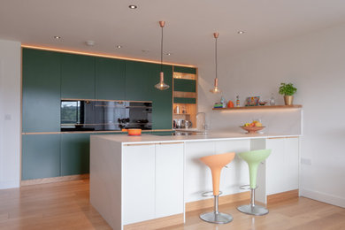 Mittelgroße Moderne Küche in U-Form mit flächenbündigen Schrankfronten, grünen Schränken, Halbinsel, schwarzen Elektrogeräten, hellem Holzboden, beigem Boden und weißer Arbeitsplatte in Hampshire