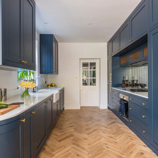Inspiration for a large traditional galley kitchen/diner in London with a belfast sink, shaker cabinets, blue cabinets, composite countertops, mirror splashback, stainless steel appliances, no island and white worktops.