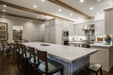 Example of a mid-sized classic u-shaped dark wood floor eat-in kitchen design in Dallas with a farmhouse sink, raised-panel cabinets, gray cabinets, marble countertops, gray backsplash, stone tile backsplash, stainless steel appliances and an island